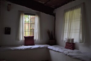 A room with two beds, a window with bars, and a wall-mounted switch.