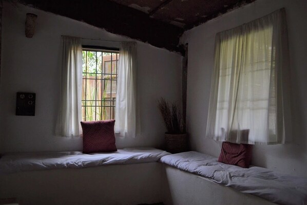 A room with two beds, a window with bars, and a wall-mounted switch.
