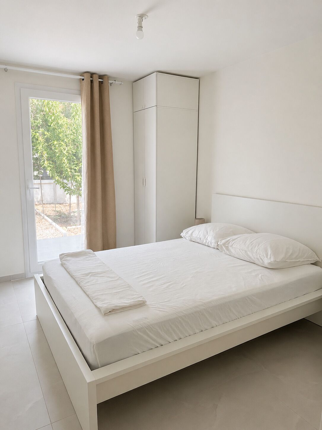 Een slaapkamer met een bed, gordijnen, een kledingkast en uitzicht op groen.