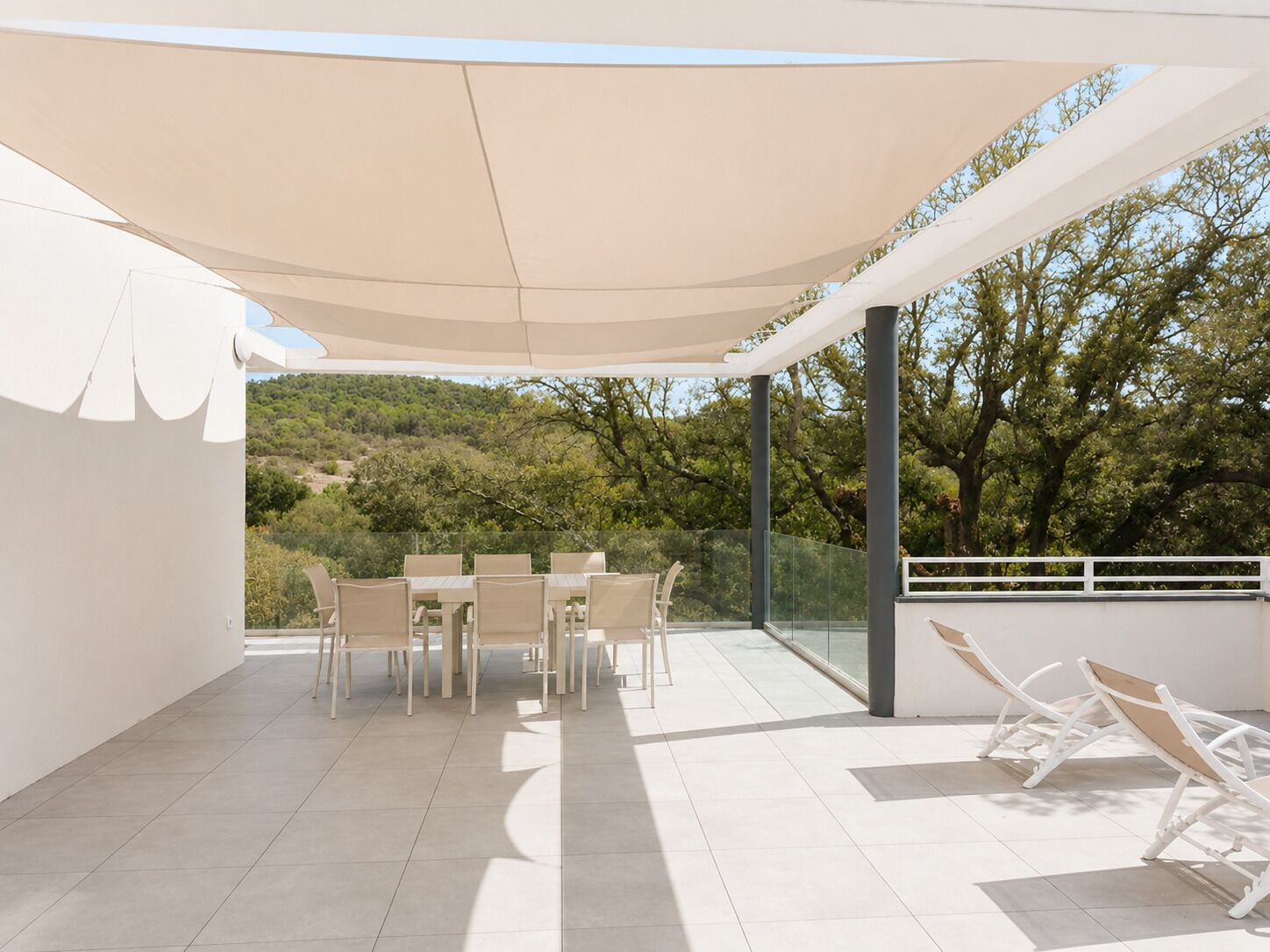 An outdoor patio with a table and chairs, a glass balustrade, and a view of trees and hills.