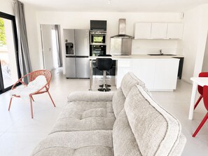 A modern kitchen with stainless steel appliances, a dining area with a white table and red chairs, and a grey sofa in the foreground. - 3-bedroom apartment measuring 86 m², with a 70 m² rooftop terrace and a private pool (Saint-Raphaël)