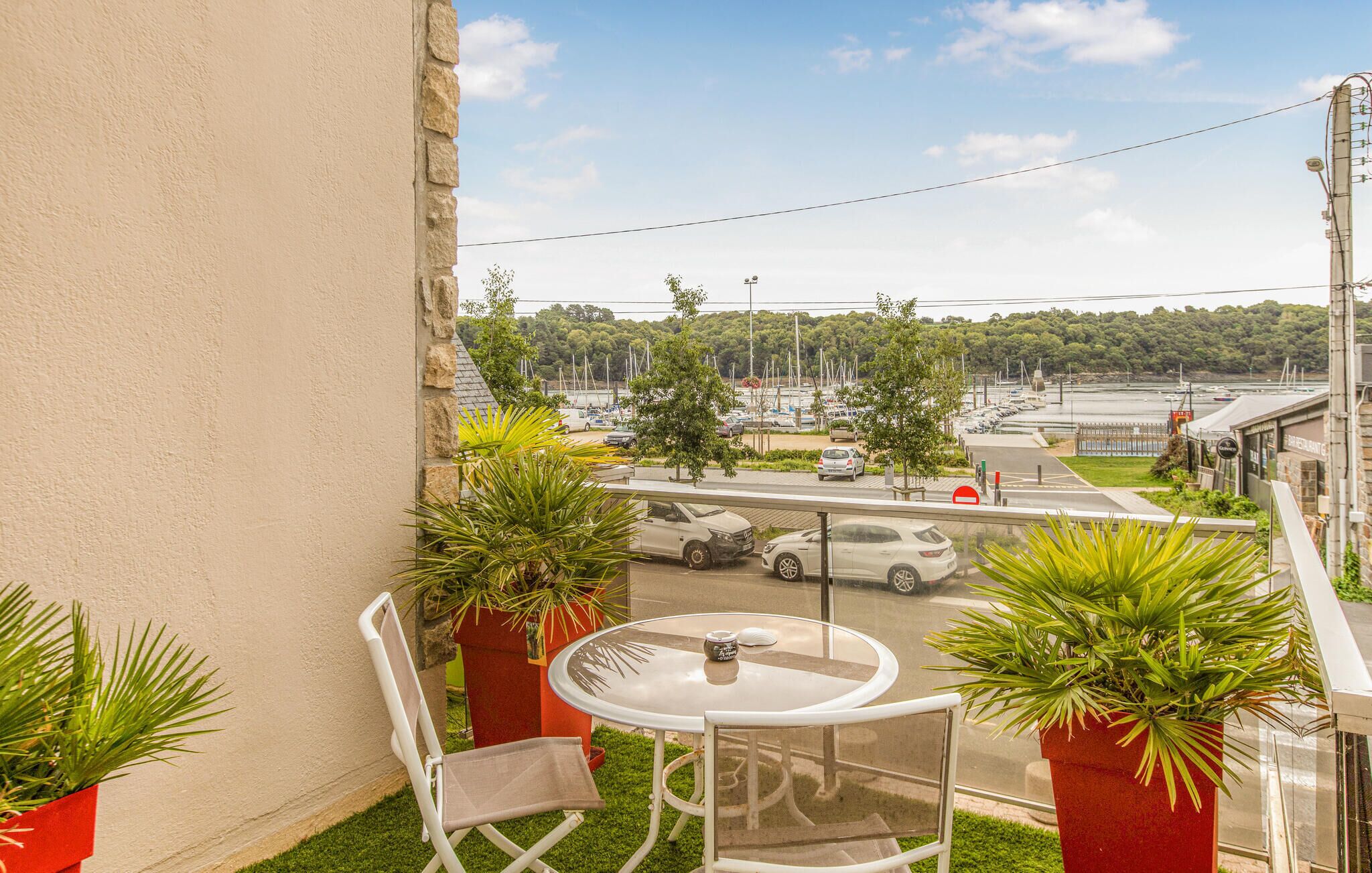 A balcony with a table and chairs, overlooking a street with parked cars and a restaurant.