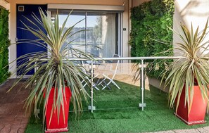 A modern outdoor area with artificial grass, two large potted plants, a metal railing, and a blue door. - Apartment in Lezardrieux (887) (Lezardrieux)