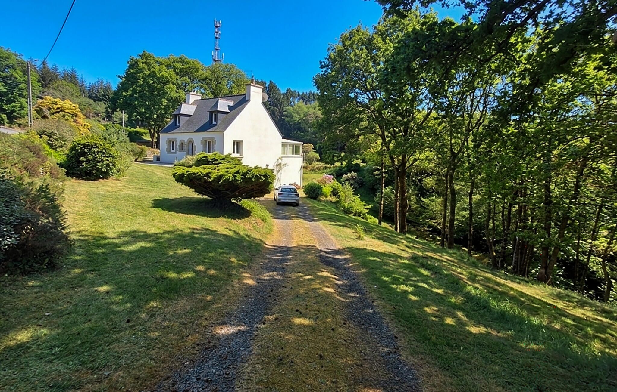 A white house with a sloped roof, a gravel driveway, and a car parked in front.
