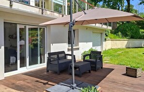 En udendørs terrasse med et bord, stole og en stor parasol, samt en skydedør til et rum.