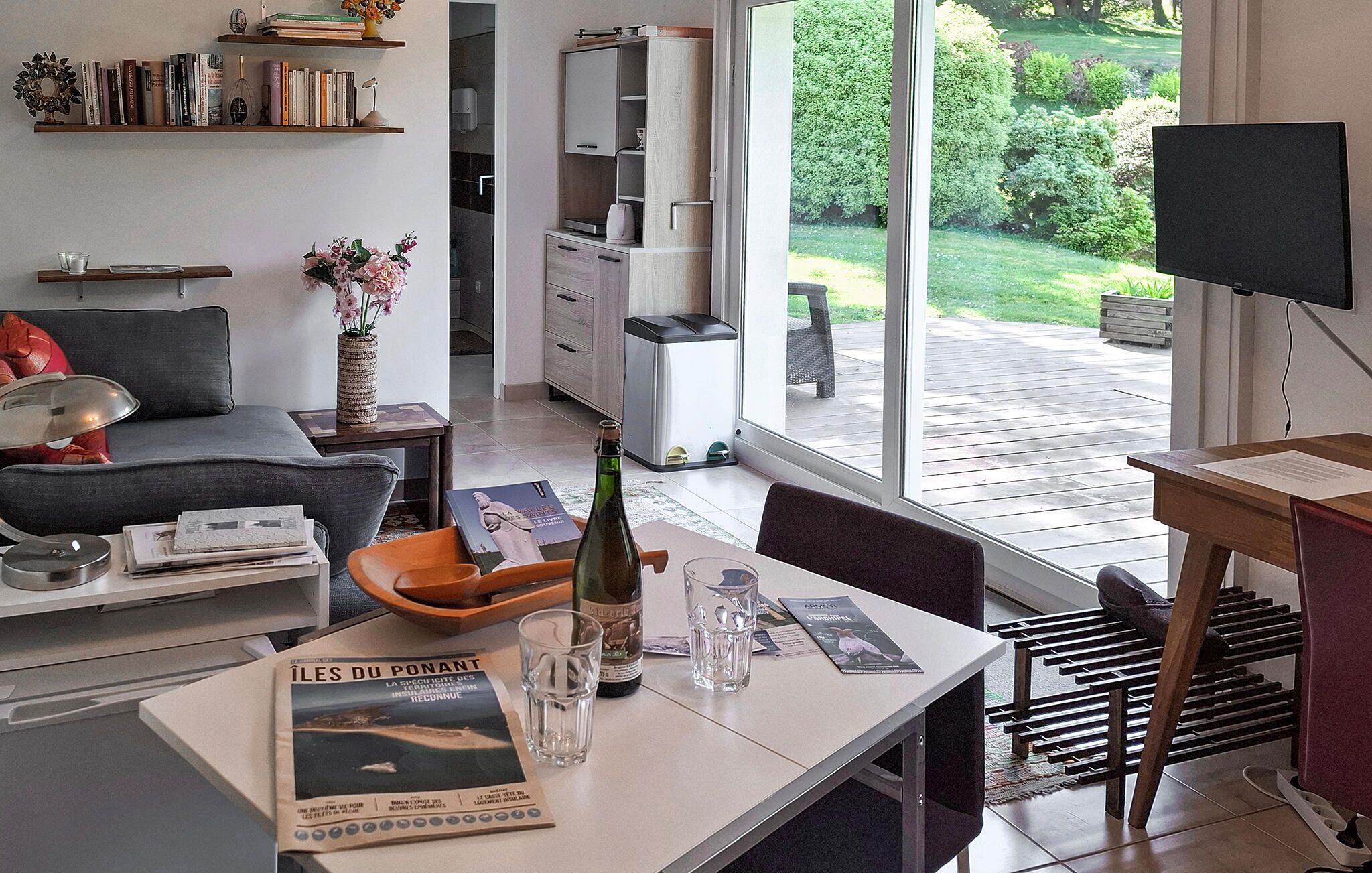 Una sala de estar moderna con comedor, estantería y vistas a un jardín a través de amplios ventanales.