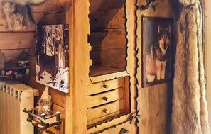 Ein rustikales Holzinterieur mit einem Regal, das ein gerahmtes Bild trägt, einer kleinen Holzkabine mit Schubladen und einem dekorativen Gegenstand auf dem Boden.