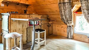 L’intérieur d’un chalet rustique en bois, avec une table en bois, un tabouret de bar et un fauteuil recouvert de fourrure.