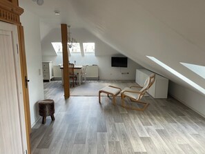 A spacious attic room with a sloped ceiling, a dining area with a table and chairs, a television mounted on the wall, and a large window allowing natural light. - Accommodations in a Hiking Paradise (Neuleiningen)