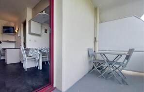 A room with a dining table and chairs, a small kitchenette, and a television mounted on the wall. - Studio piscine proche plage (La Rochelle)