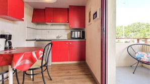 A compact kitchen with red cabinets, a small dining table, and a chair. - Studio piscine proche plage (La Rochelle)
