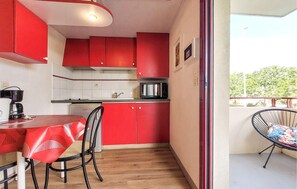 A compact kitchen with red cabinets, a small dining table, and a chair. - Studio piscine proche plage (La Rochelle)