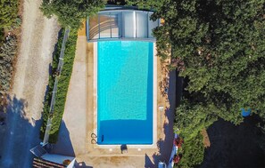 Vista aerea di una piscina rettangolare con superficie d'acqua cristallina e blu, circondata da un solido bordo in cemento e ornata da una vegetazione lussureggiante.