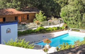 Ein Poolbereich mit einem Holzhaus, einem eingezäunten Garten und einem kühlen, blauen Pool.