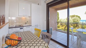 Une cuisine moderne avec des meubles blancs, une table à manger recouverte d’une nappe à motifs et une vue sur un balcon agrémenté d’une table et de chaises.