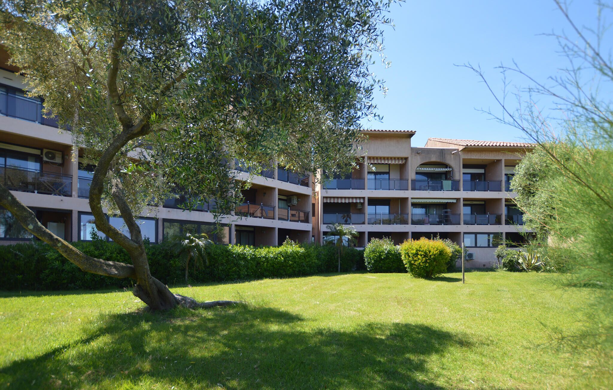 A multi-story hotel with balconies, surrounded by well-maintained grass and trees.