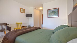 Une chambre à coucher comprenant un lit, une chaise, un bureau, un téléviseur et deux tableaux encadrés accrochés aux murs.