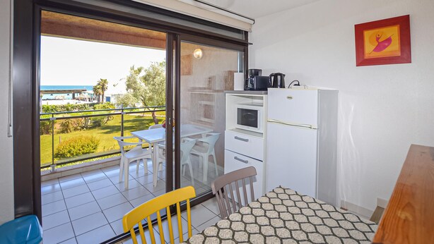 Un balcon avec une table et des chaises, un réfrigérateur et une vue sur la mer.