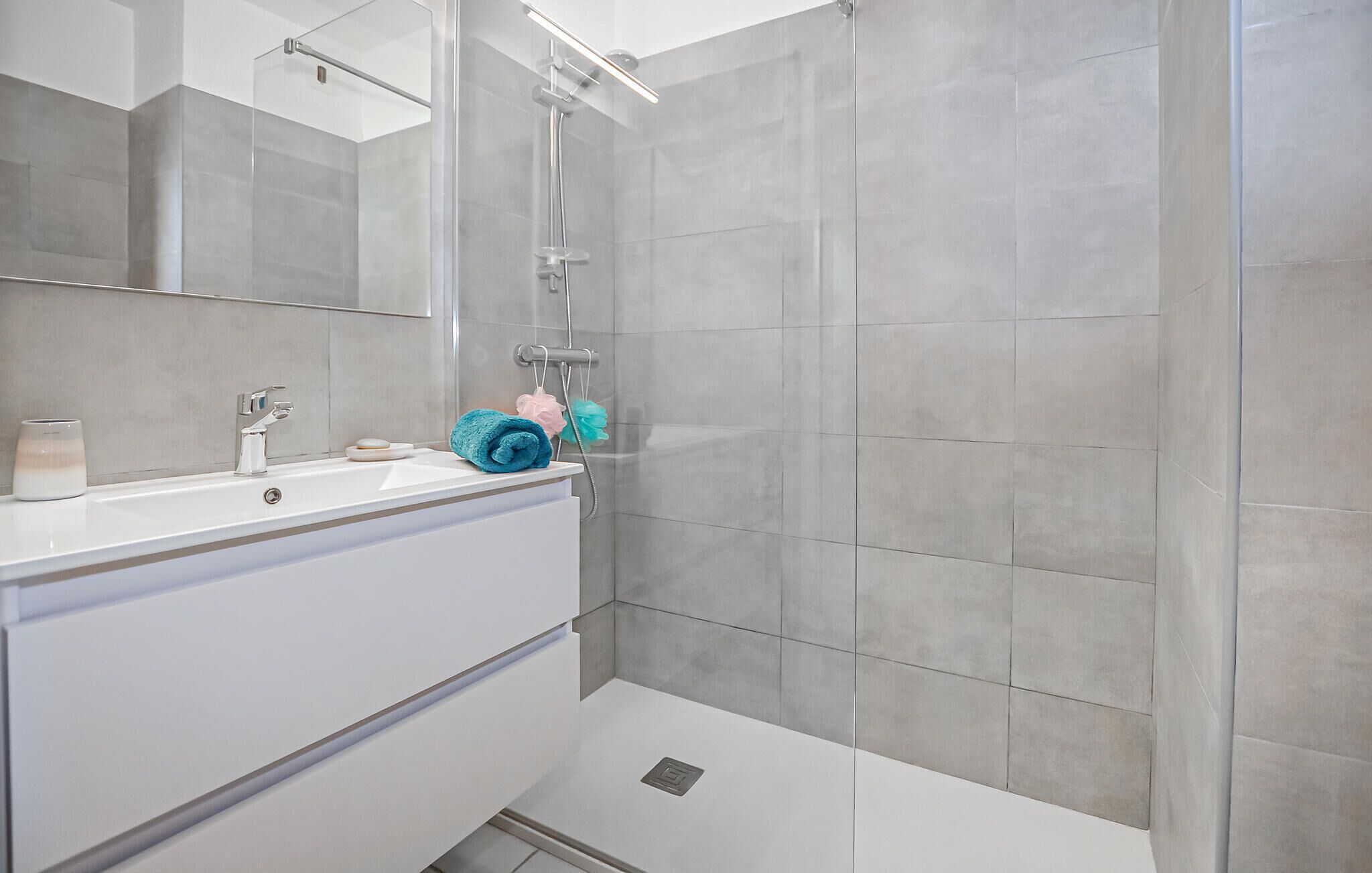 A modern bathroom with a white vanity, a mirror, and a shower area.