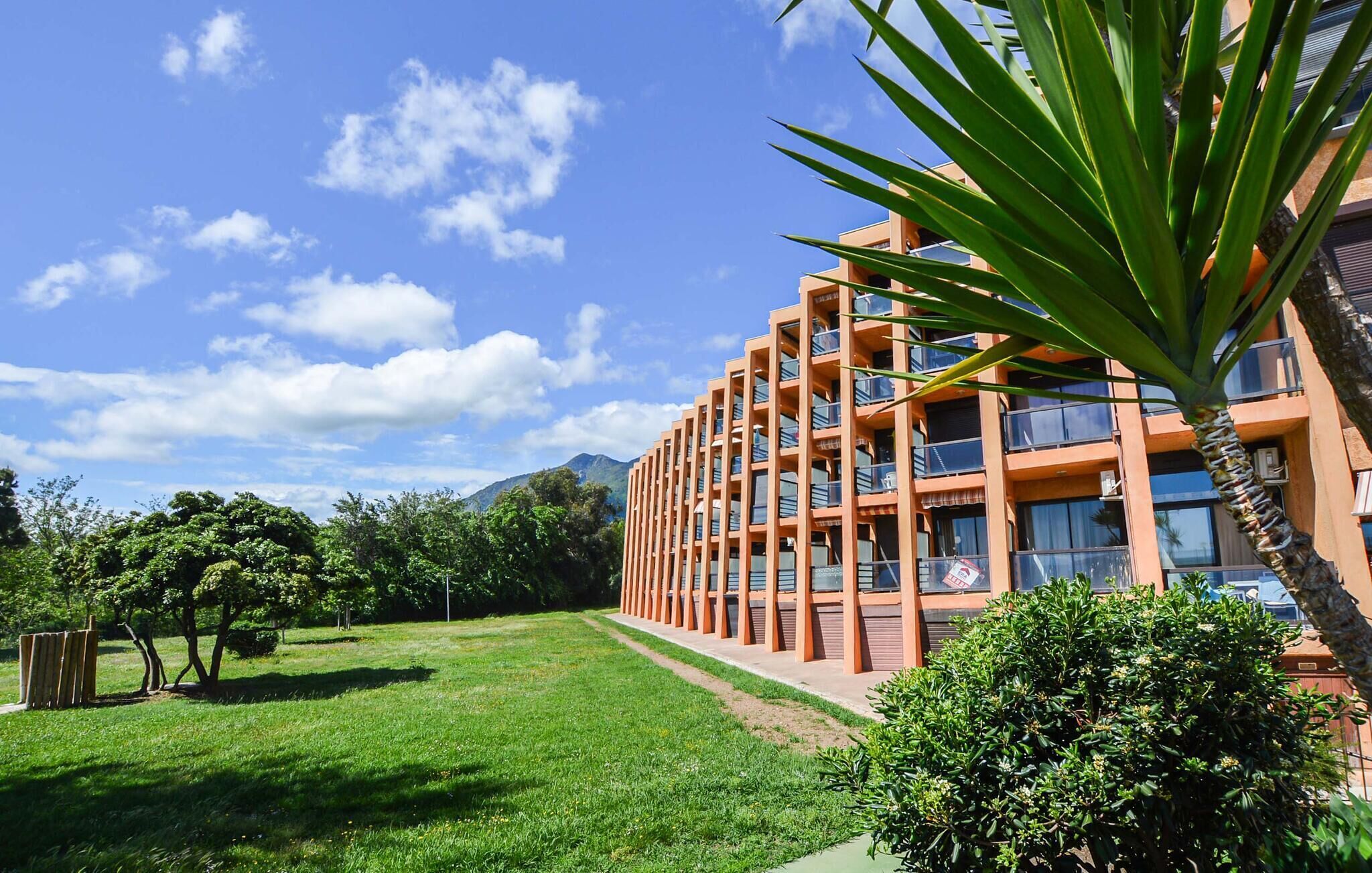 Un edificio moderno con varios balcones, rodeado de exuberante vegetación y un cielo despejado.