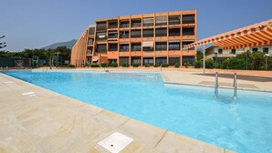 En swimmingpool med ett kaklat poolområde, en flervåningsbyggnad med balkonger och ett berg i bakgrunden.