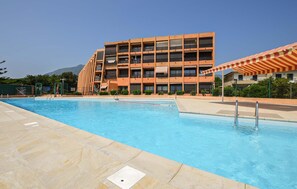 A swimming pool with a tiled deck, a multi-story building with balconies, and a mountain in the background. - Nice apartment in Ste Lucie De Moriani (Ste Lucie De Moriani)