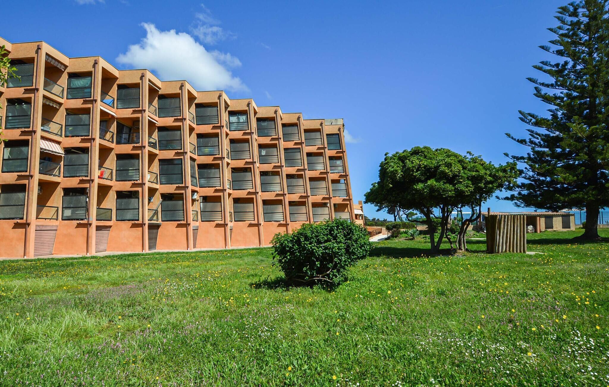 Um edifício moderno com fachada geométrica, área gramada com árvores e céu claro.
