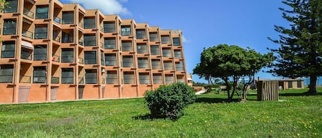 Um edifício moderno com fachada geométrica, área gramada com árvores e céu claro.