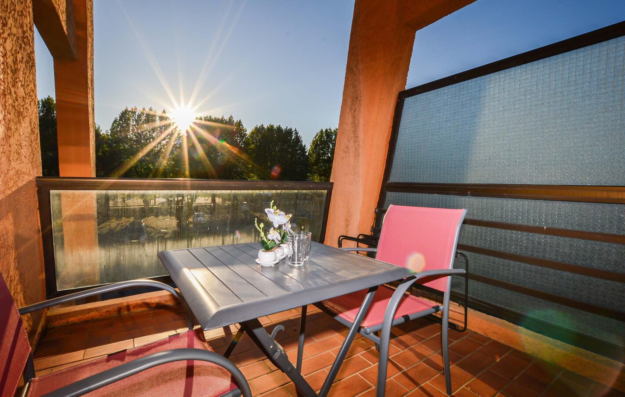 Une terrasse extérieure avec une table et des chaises, une barrière en verre et une vue sur le coucher du soleil.
