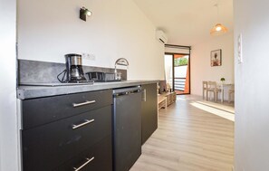 A modern kitchen with a built-in dishwasher, a coffee maker, and a sink. There is a dining area with a table and chairs visible in the background. - Nice apartment in Ste Lucie De Moriani (Ste Lucie De Moriani)