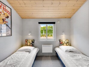 Ein Zimmer mit zwei Einzelbetten, einem Fenster mit Blick auf Grünflächen, einem Heizkörper und einem Poster an der Wand.