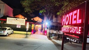Entrada de hotel com letreiro de neon, placa de estacionamento e fachada do edifício.
