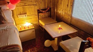 Um quarto com uma cama, uma mesa com velas, uma cadeira e uma janela com persianas.