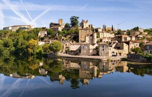 Eine historische Stadt mit Häusern, die sich im ruhigen Wasser spiegeln, umgeben von viel Grün.