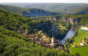 Eine historische Stadt liegt eingebettet in ein Tal, durchquert von einem Fluss, umgeben von üppiger Vegetation und steilen Felswänden.