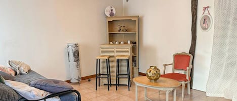 A room with a bed, a table with chairs, a bookshelf, and a chair with a red cushion.