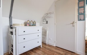 A white dresser with drawers and a shelf, a white chair, a wooden floor, and a door with a light switch and a hanging coat rack. - Close to D-Day beaches (Isigny-sur-Mer)