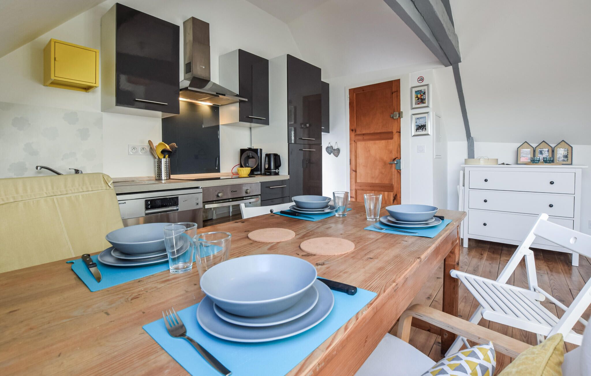 Una cocina moderna con armarios oscuros, una mesa de comedor de madera dispuesta con platos y vasos, y una silla blanca.