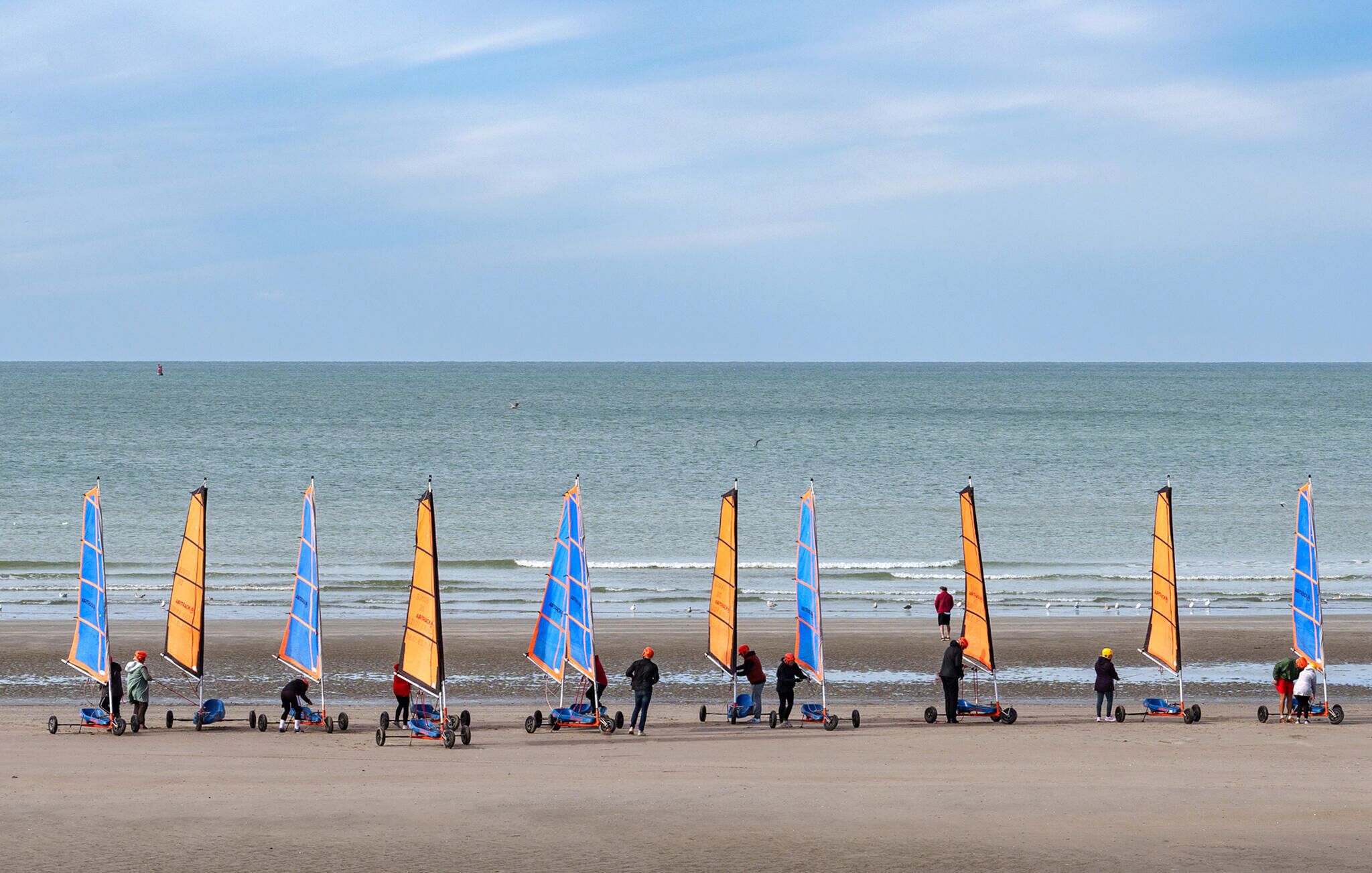 A beach with multiple windsurfing equipment and people preparing for the activity.