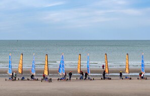 Une plage où l’on trouve de nombreux équipements de planche à voile et où des personnes se préparent à pratiquer cette activité.