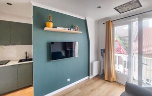 A modern living room with a flat-screen TV mounted on a teal wall, a wooden floor, and a sliding glass door leading to an outdoor area. - Studio en plein centre-ville (Le Touquet-Paris-Plage)