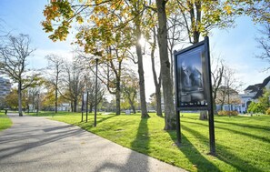 En park med en asfalterad gångväg, träd med höstlöv och en affisch på en stolpe.