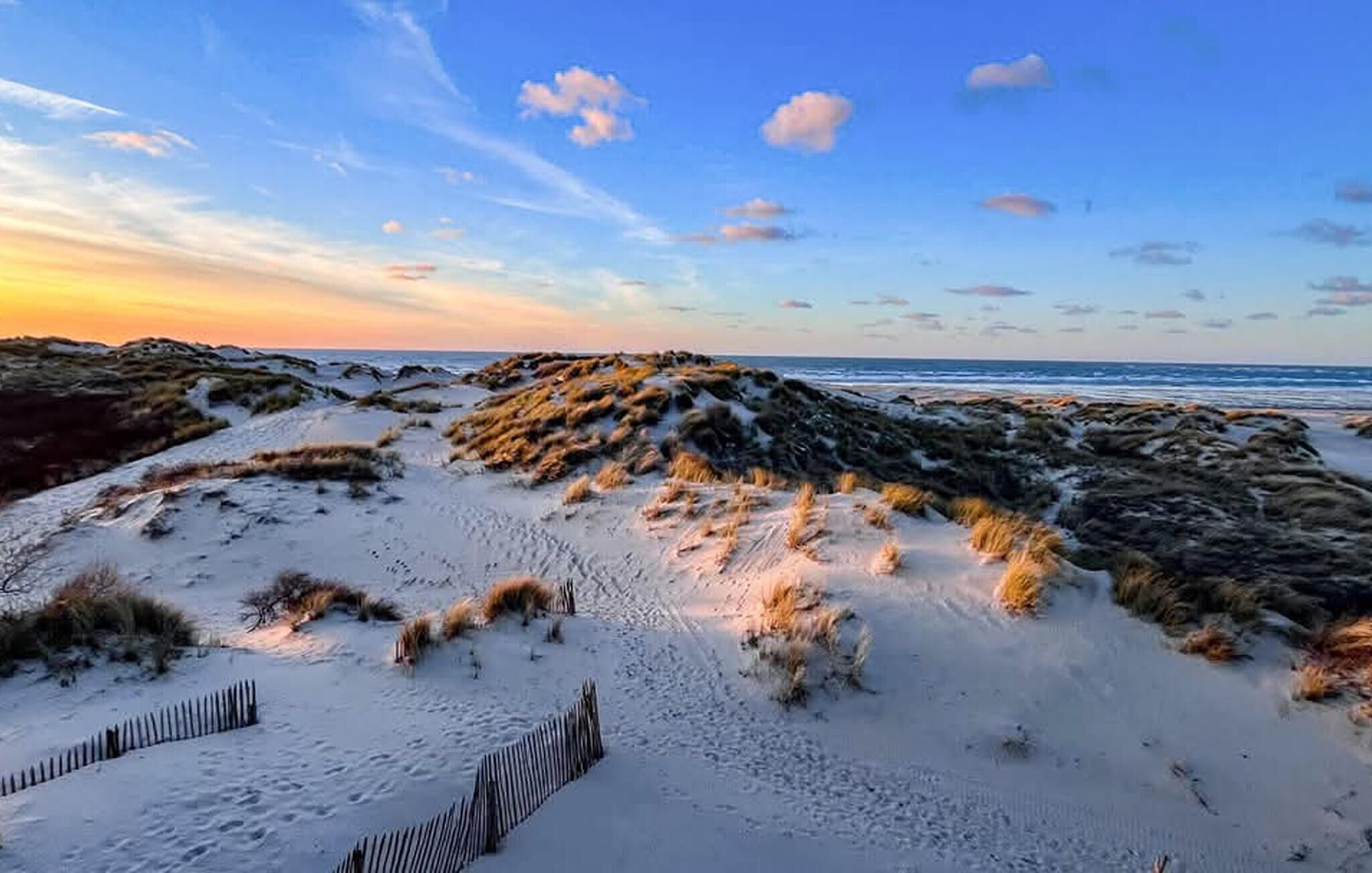 Ein Strand mit Sanddünen und einem Holzzaun.