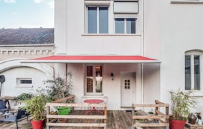 A white building with a red awning, a wooden table with chairs, and potted plants. - Lovely home in Huby Saint Leu with WiFi (Huby Saint Leu)