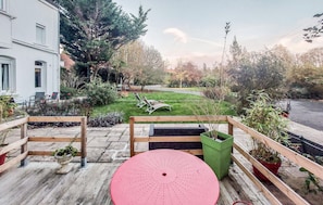 A wooden deck with a red circular table, a green planter, and a white building in the background. - Lovely home in Huby Saint Leu with WiFi (Huby Saint Leu)