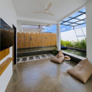 A modern interior with a ceiling fan, a wooden fence, a glass enclosure, and a seating area with cushions. - Altura Esthetic Villas (Batam)