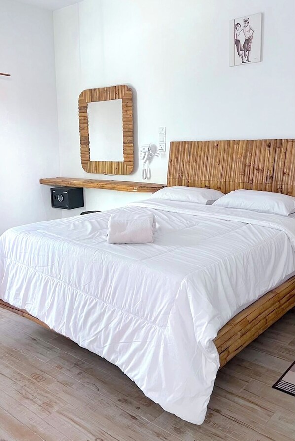 A bed with white bedding, a wooden headboard, a bedside table with a lamp, and a wall-mounted mirror. - Altura Esthetic Villas (Batam)