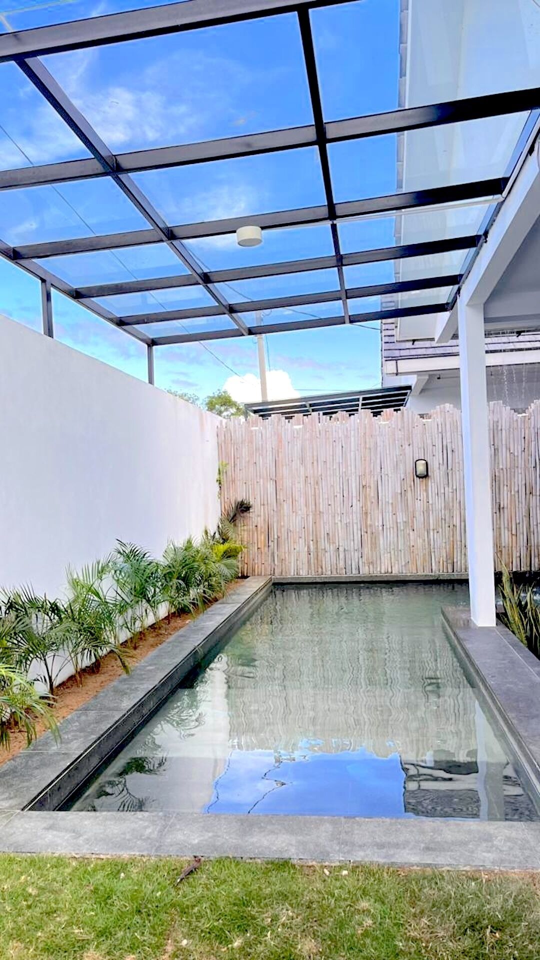 A swimming pool with a glass enclosure, surrounded by a wooden fence and greenery.