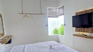 A hotel room with a bed, a TV, a window with blinds, and a wooden shelf. - Altura Esthetic Villas (Batam)