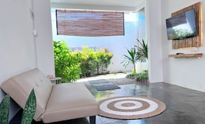 Una sala moderna con un sofá, un televisor montado en la pared y vistas a un jardín.